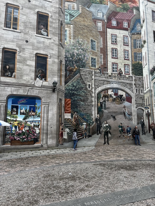 A stone street with a stone building next to a very tall mural that makes it look like the stone street keeps going