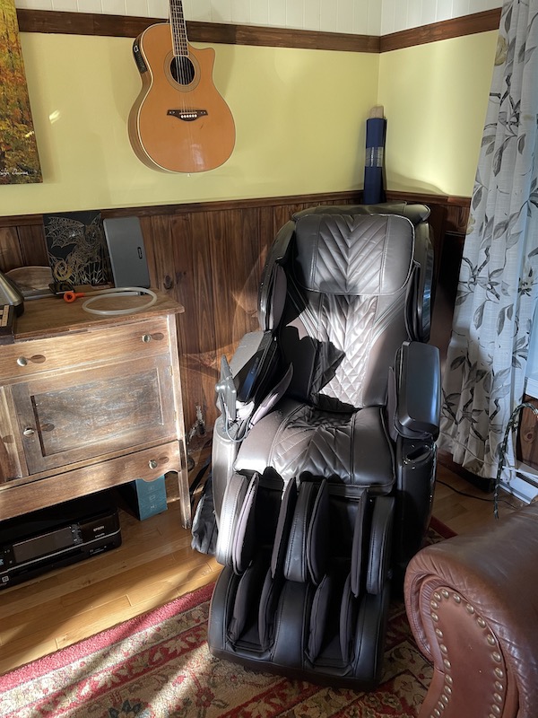 A corner of a room at the cousin's house in Saguenay featuring a guitar on the wall and a complex looking leather massage chair