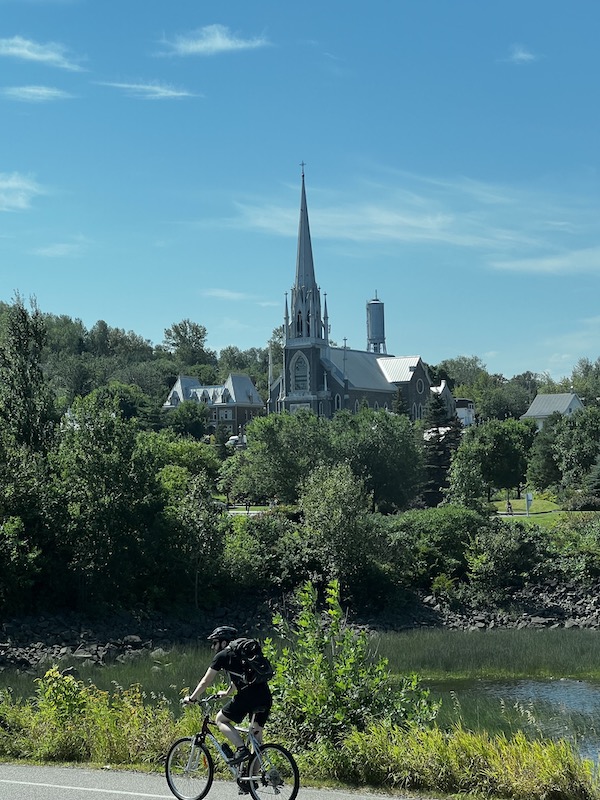 A tall skinny church beyond a river