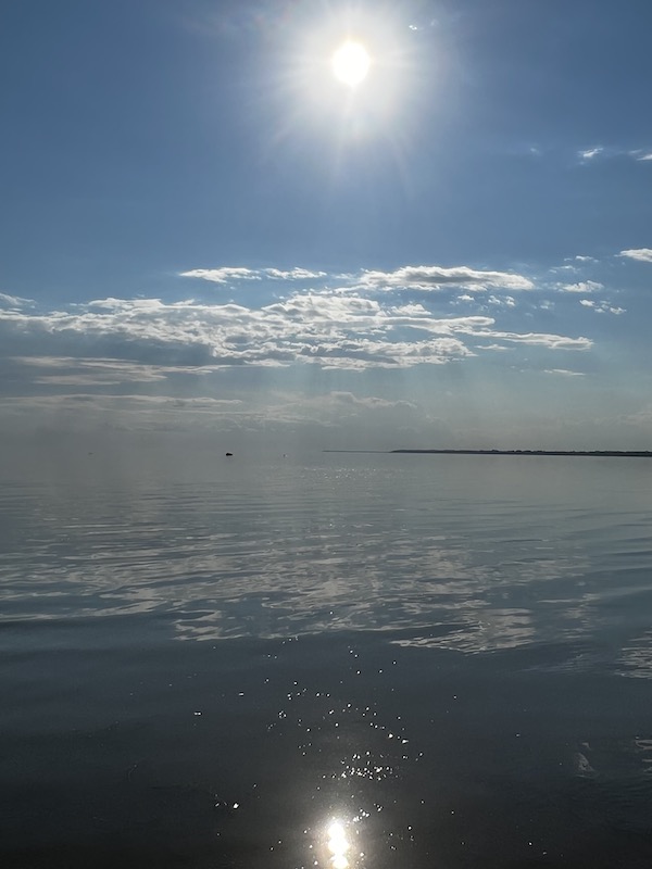 Calm lake water meeting a skyline, with the sun reflecting and the fog blurring the line where the water and sky meet